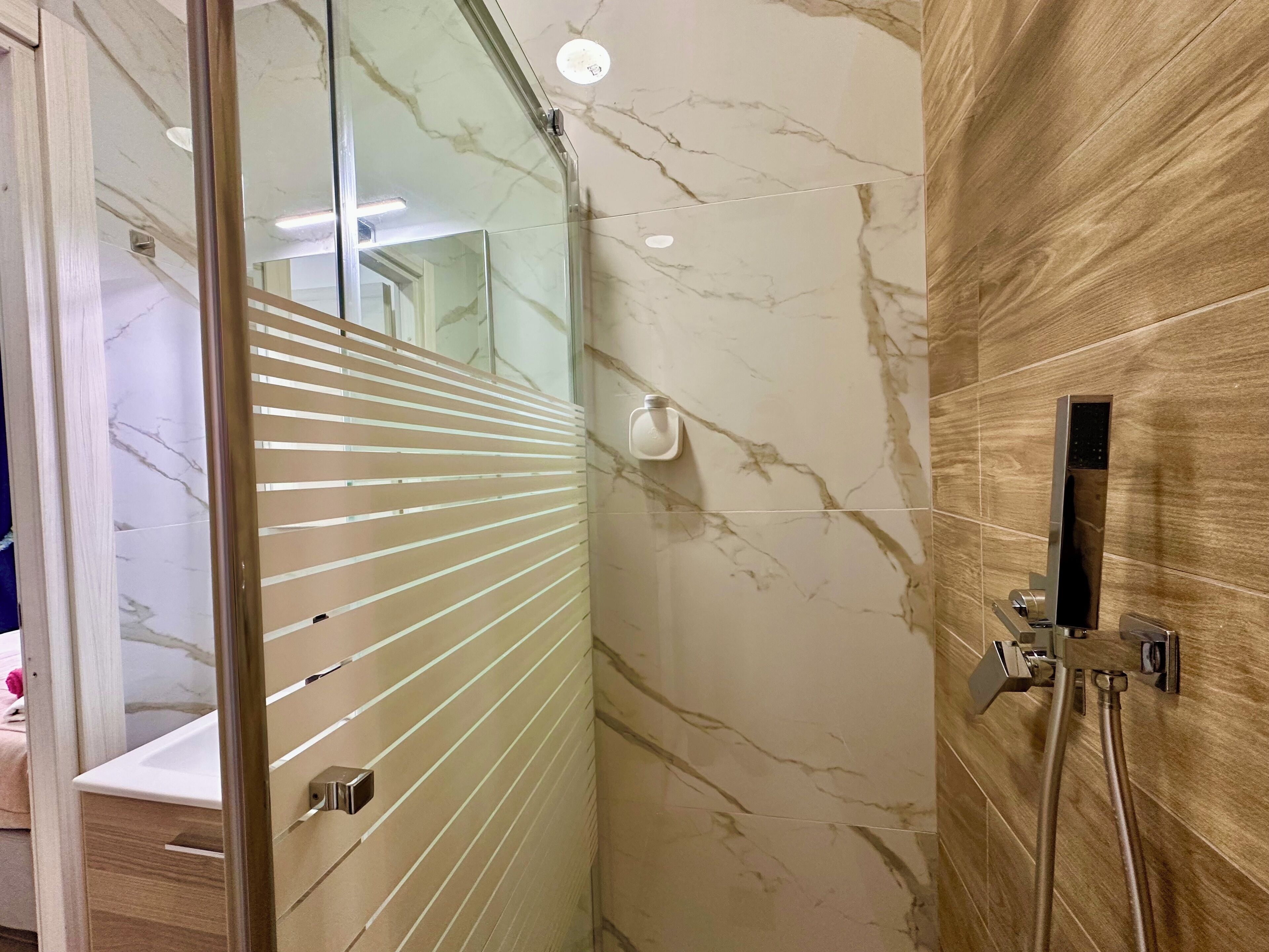 A bathroom with a glass door, a shower area, and a marble wall.