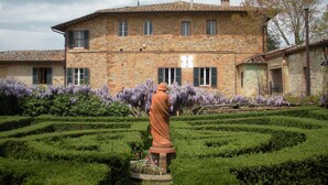 A stone building with a clock, surrounded by a well-manicured garden with purple flowers. - Agriturismo Fattoria Del Colle (Trequanda)