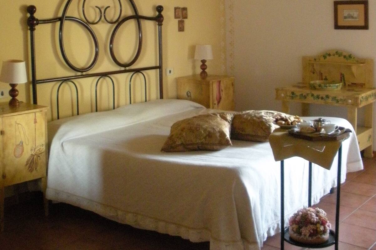 A bedroom with a bed, a bedside table with a lamp, a small table with a basket, and a hanging light fixture.