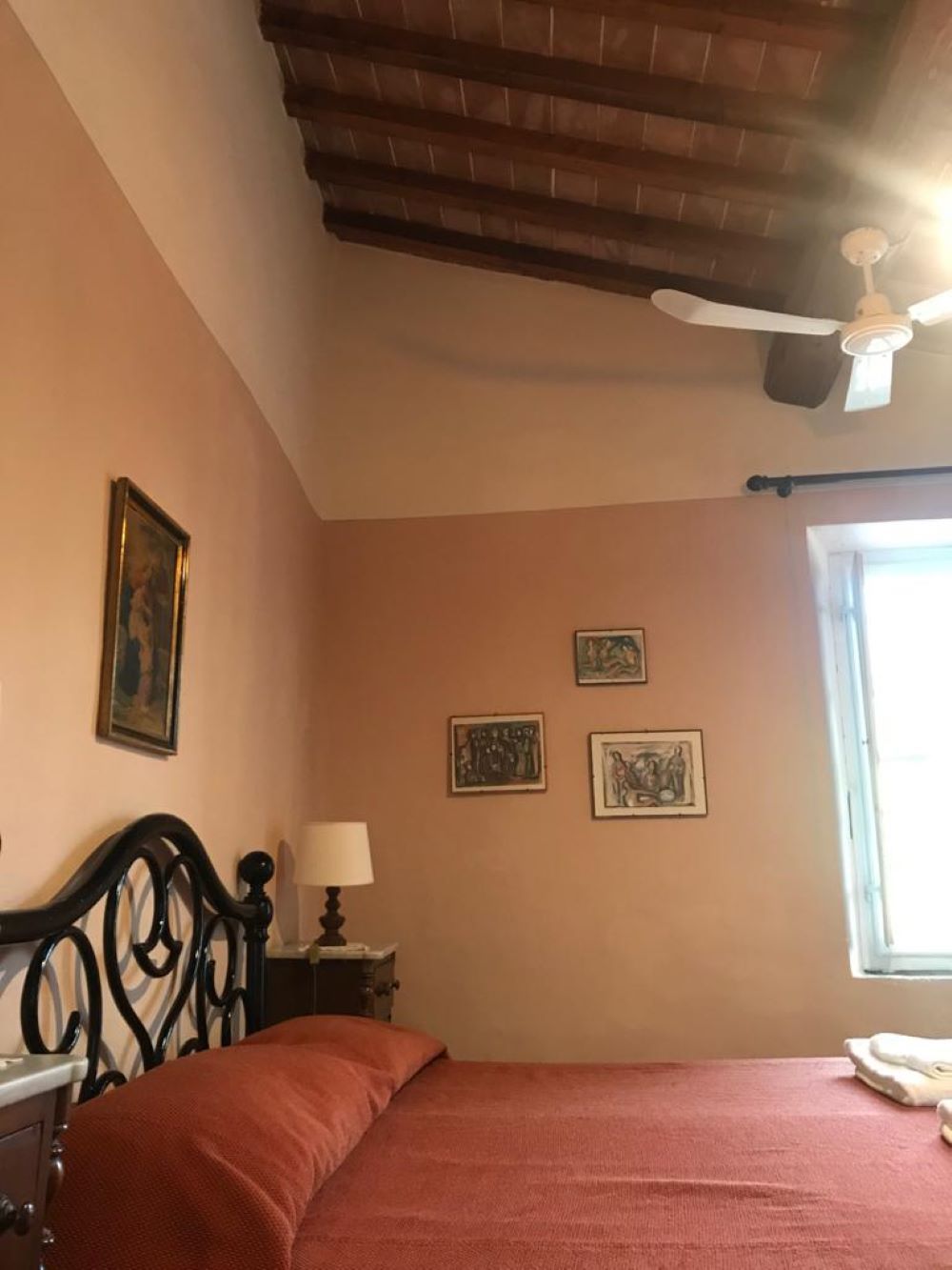 A bedroom with a bed, a ceiling fan, a window, and wall-mounted artwork.
