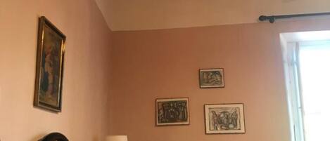 A bedroom with a bed, a ceiling fan, a window, and wall-mounted artwork.