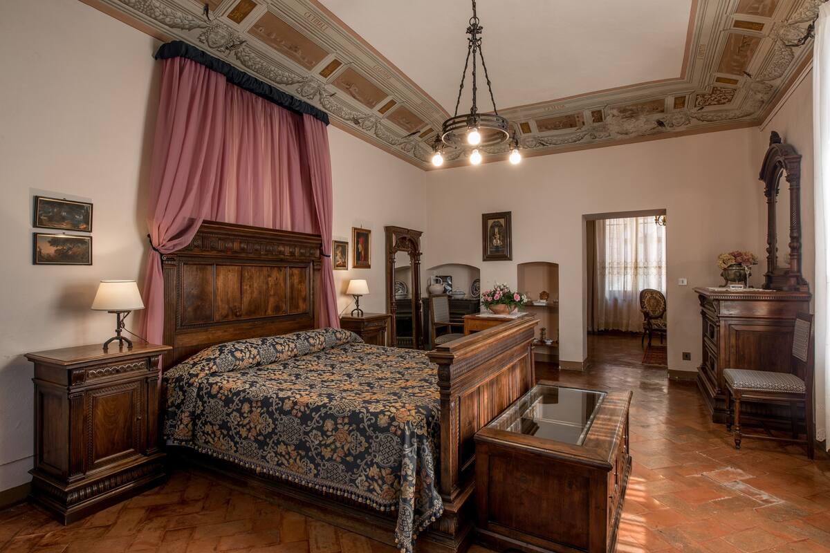 A traditional bedroom with a large bed, wooden furniture, and a classic ceiling design.