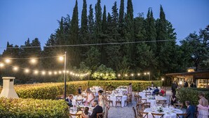 An outdoor dining area with round tables and chairs, surrounded by greenery and string lights. - Agriturismo Fattoria Del Colle (Trequanda)