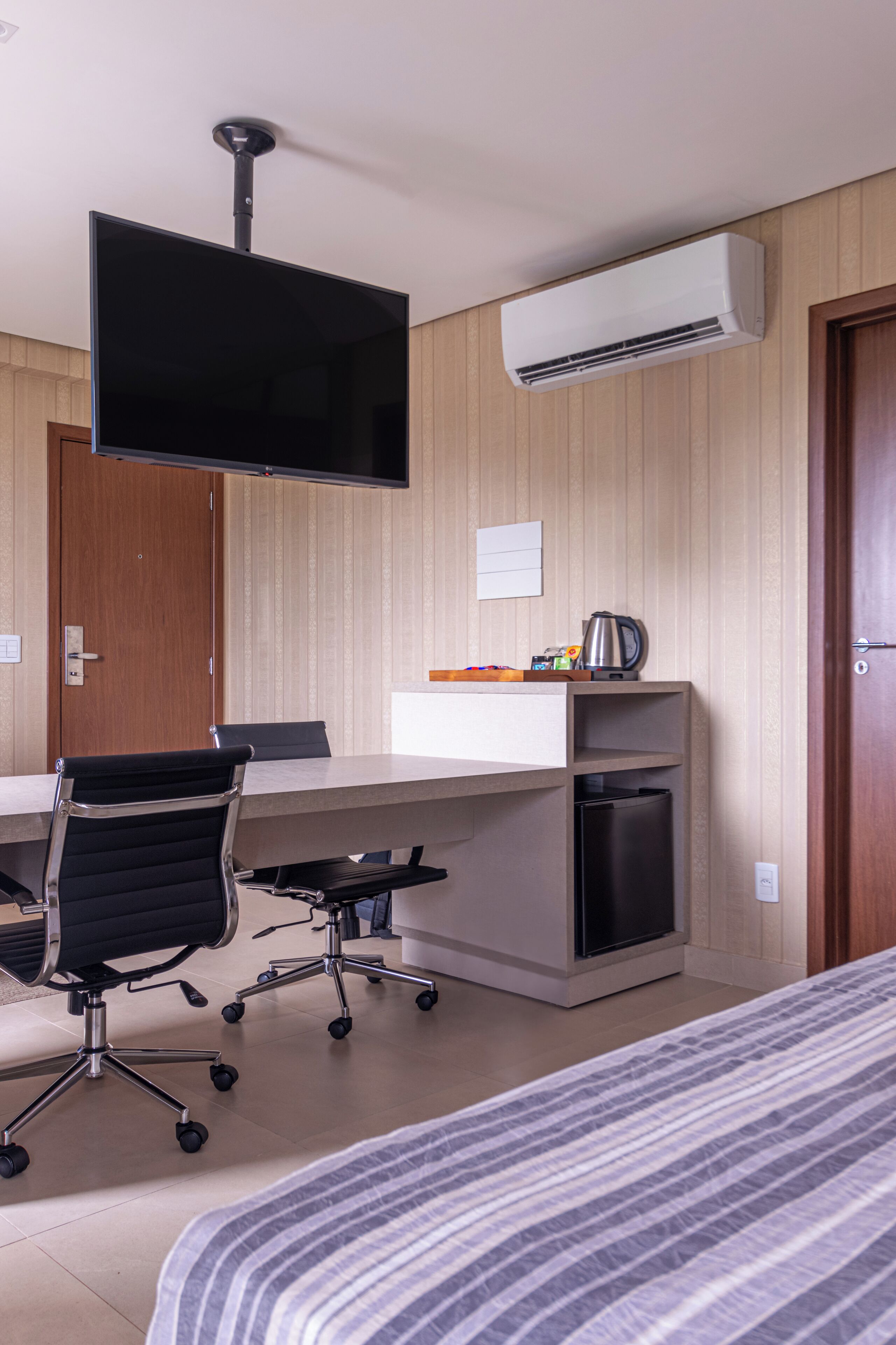 Una habitación de hotel con cama, escritorio con silla, televisor de pantalla plana, aire acondicionado y cafetera.