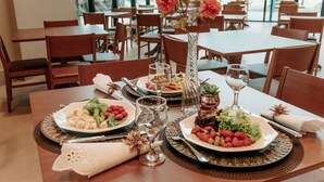 A dining table set with plates of food, glasses, and cutlery in a restaurant with wooden chairs and large windows.
