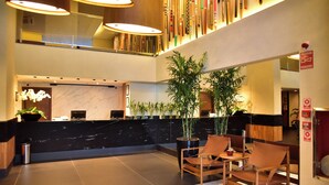 A hotel lobby with a reception desk, seating area, and potted plants.