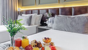 A hotel room with a neatly made breakfast tray on the bed, a bedside table with a lamp, and a modern headboard.