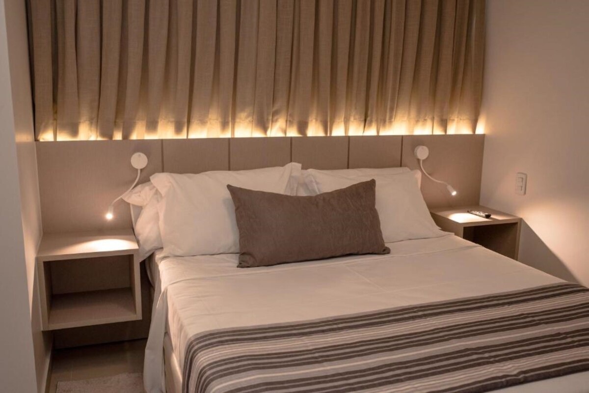 A modern bedroom with a bed, two bedside tables, and a headboard with integrated lighting.
