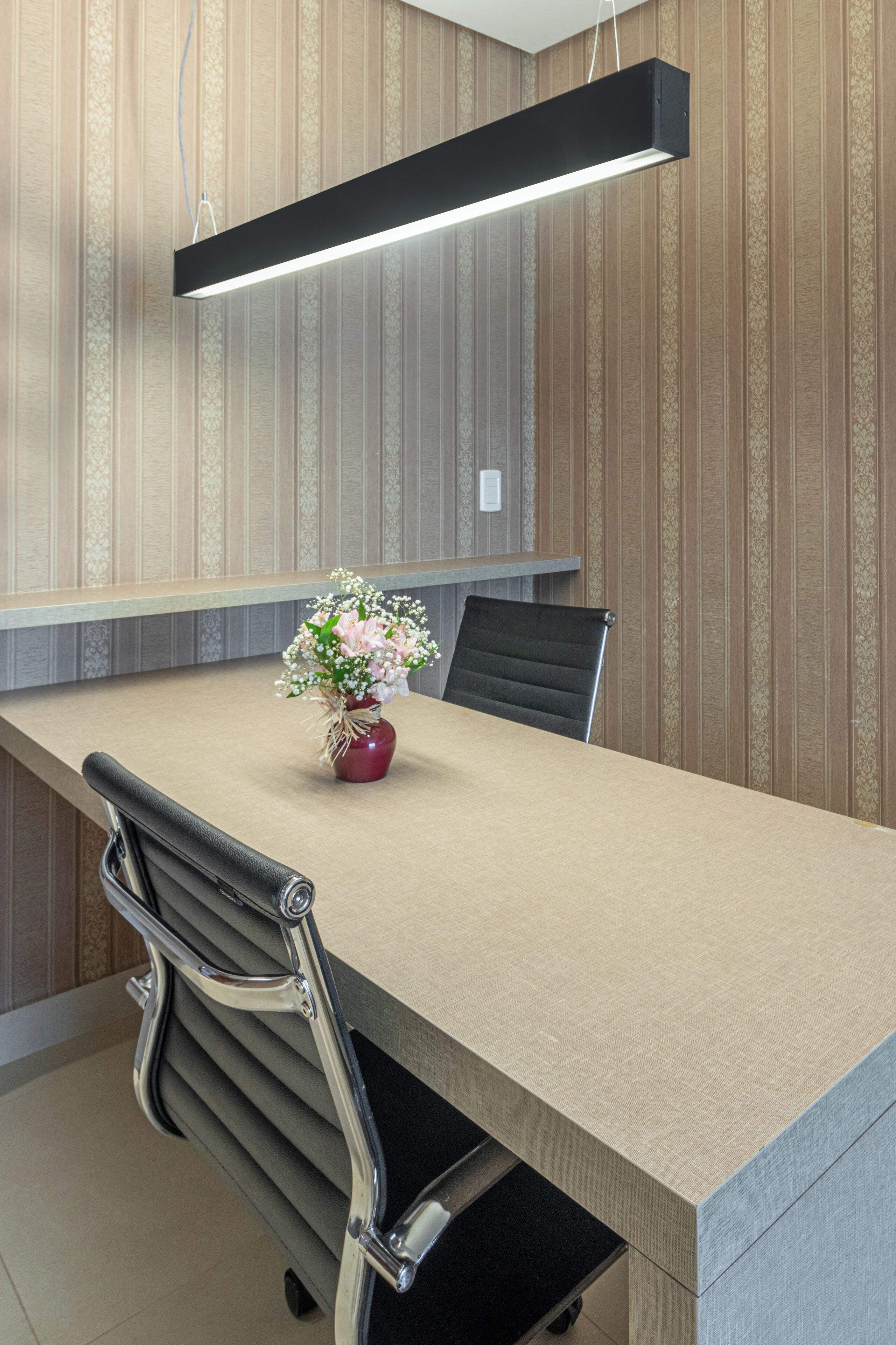 A conference room with a long table, chairs, a vase with flowers, and a hanging light fixture.