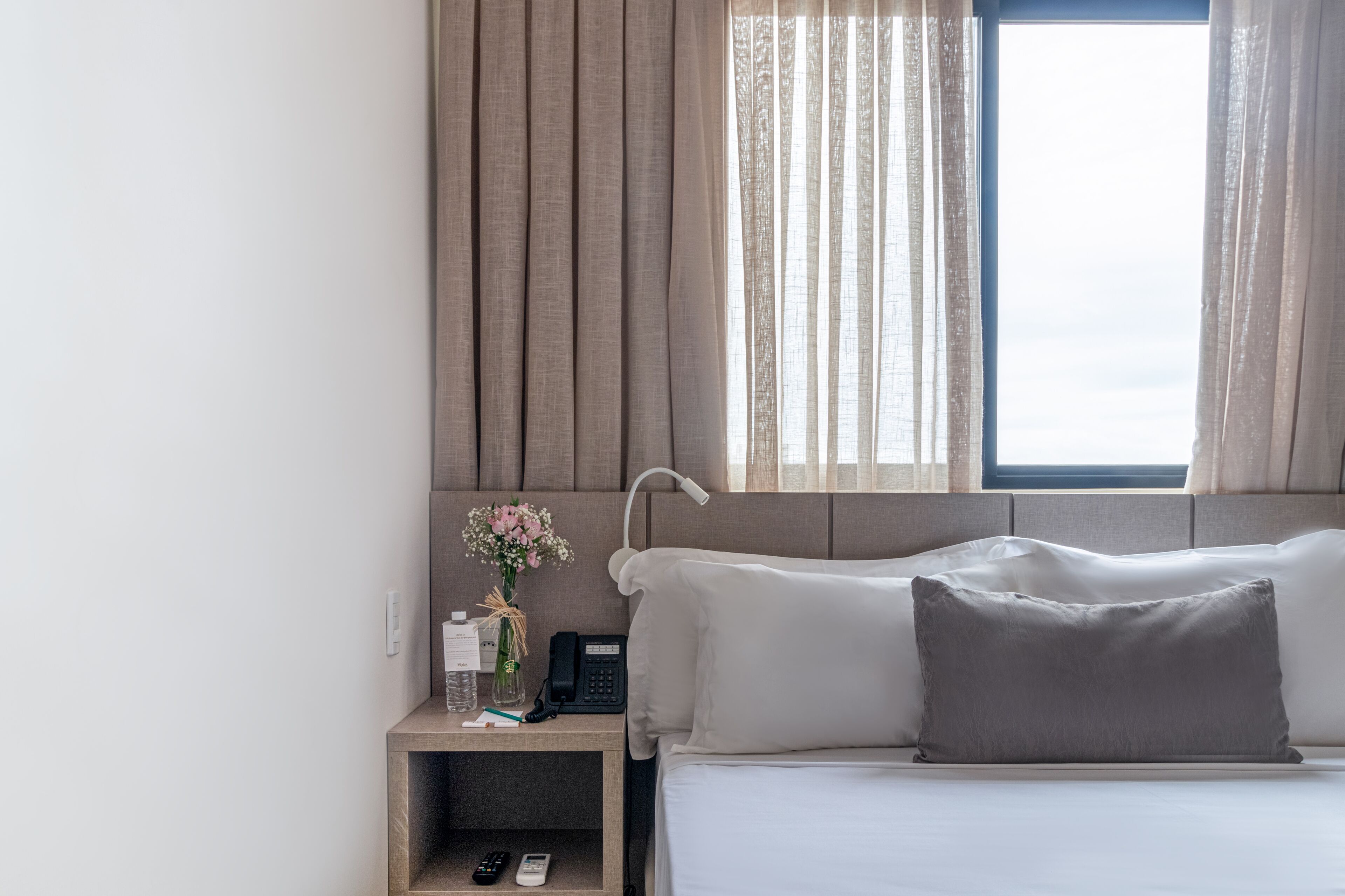 A hotel room with a bed, bedside table, lamp, and a window with curtains.
