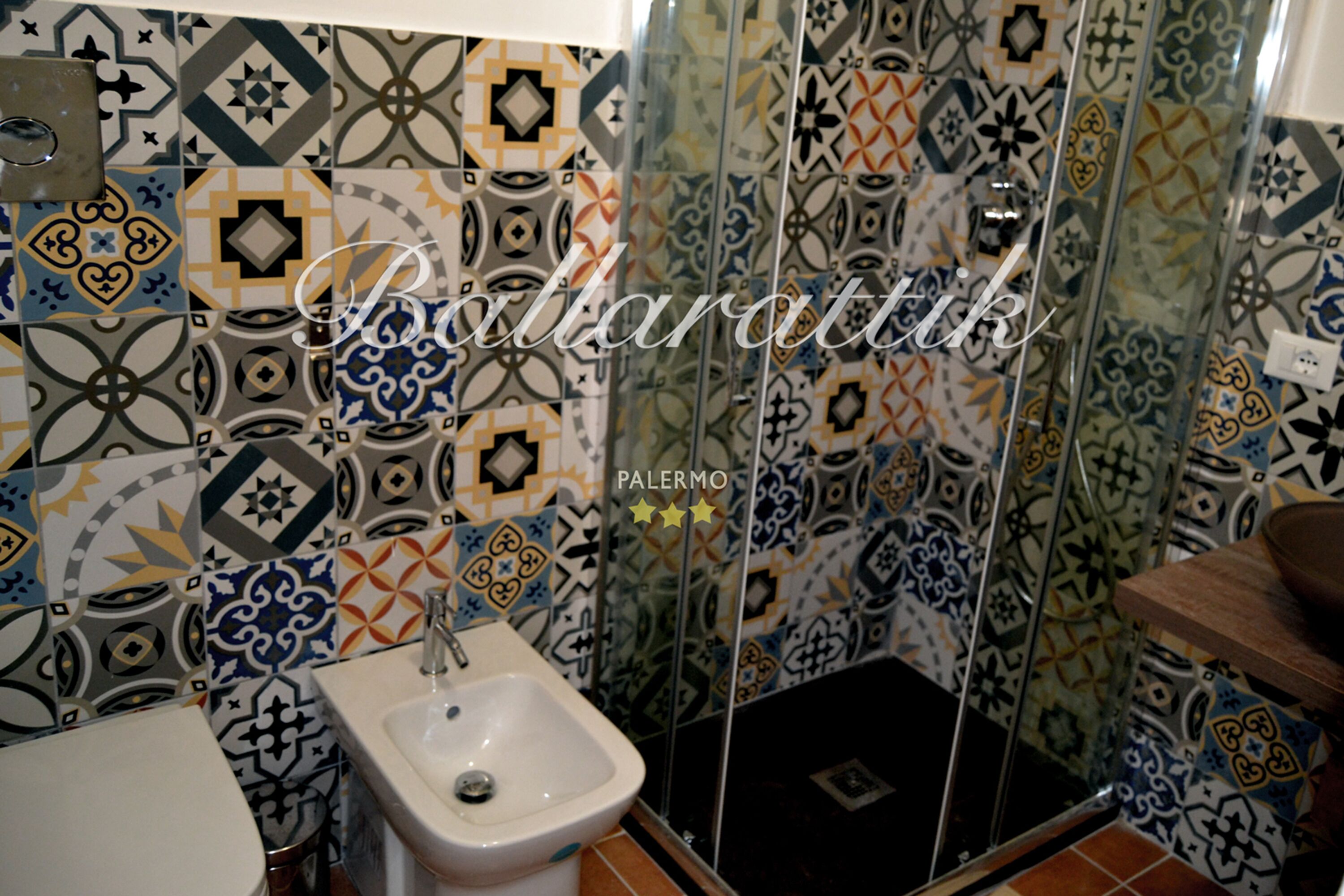 Bagno con lavandino bianco, bidet e zona doccia. Le pareti sono rivestite con diversi motivi geometrici.