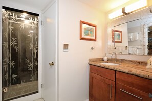 Ein Badezimmer mit Glastür, Waschbecken mit Marmorplatte, Holzschränken, einem gerahmten Bild an der Wand und einem großen Spiegel.