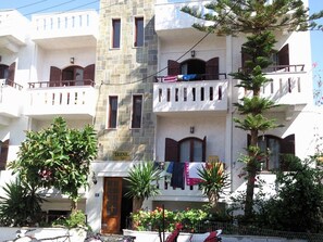 A multi-story building with balconies, a sign reading "Irene Apts", and various plants and flowers around the entrance. - Irene Apartments (Hersonissos)