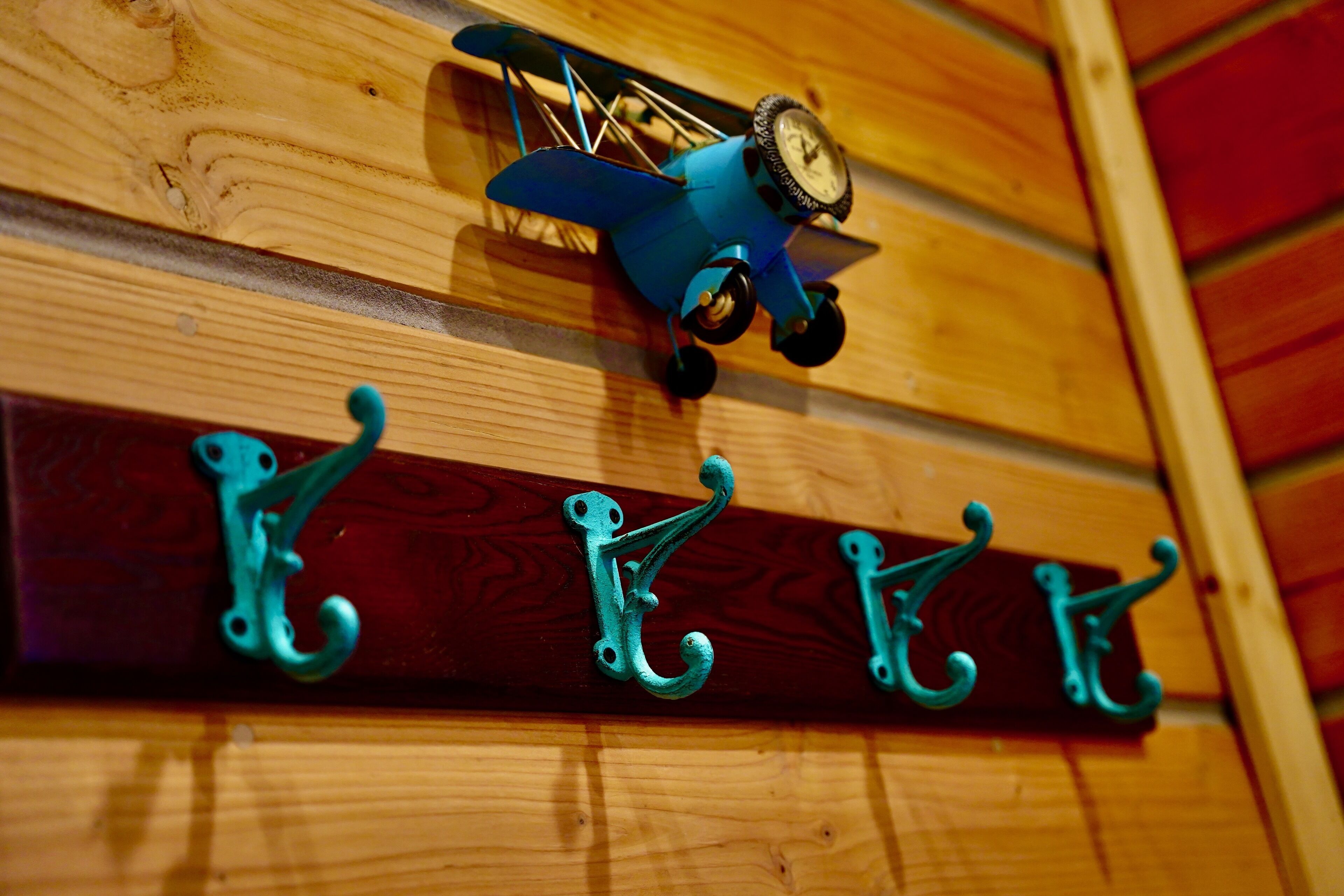 A wooden wall with a clock and three metal hooks.