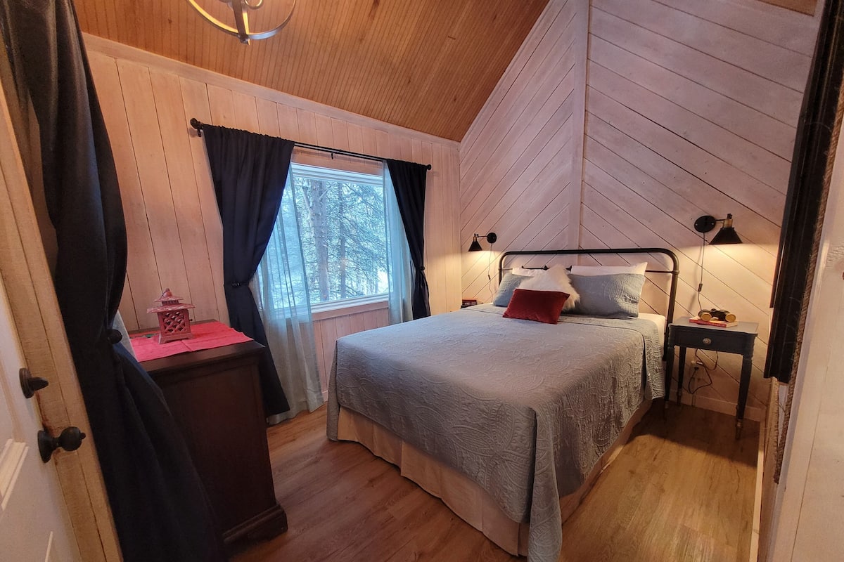 A bedroom with a bed, a nightstand, a lamp, and a window with curtains.
