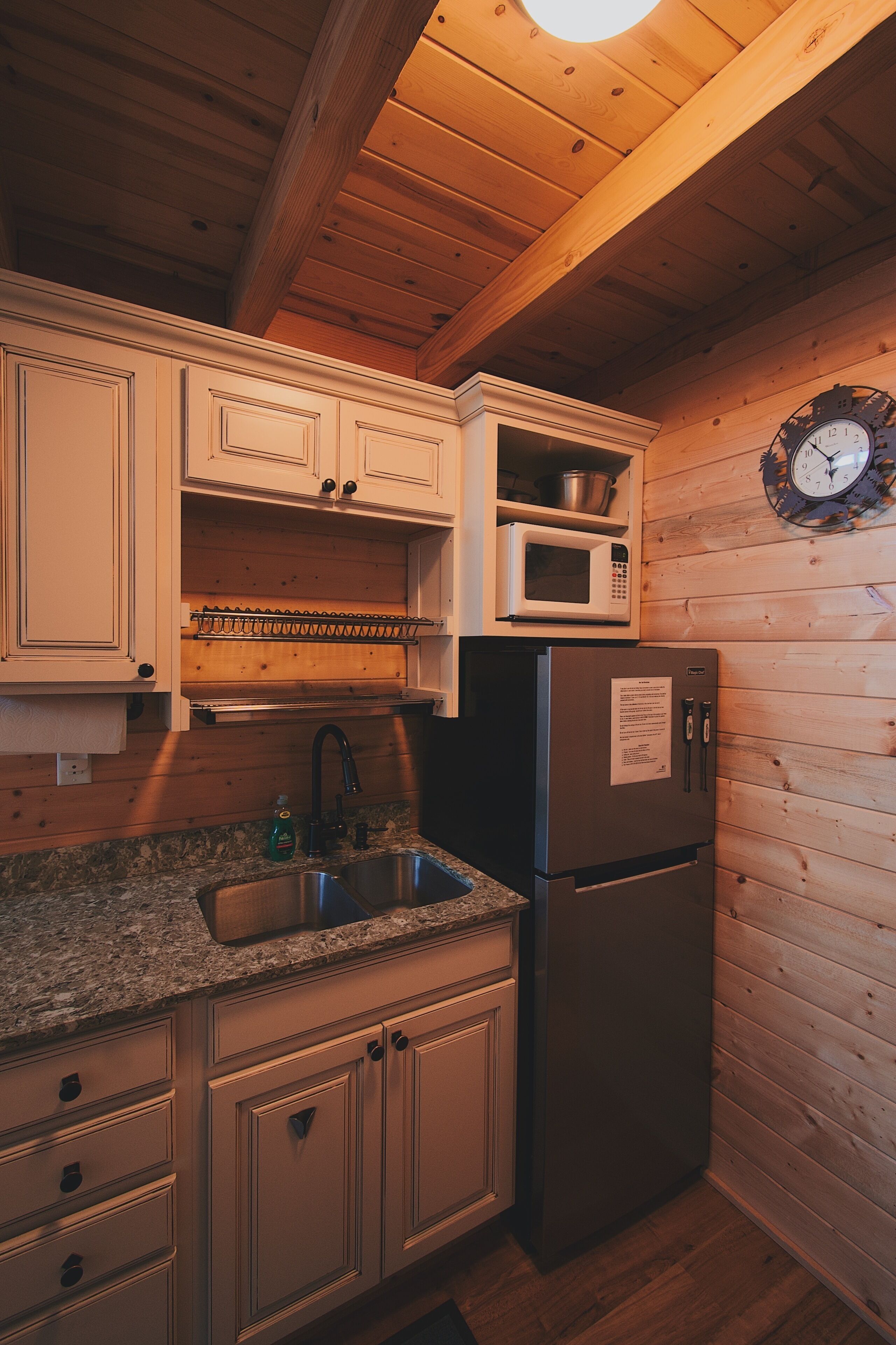 Cocina compacta con armarios de madera, refrigerador de acero inoxidable, microondas y un lavamanos.