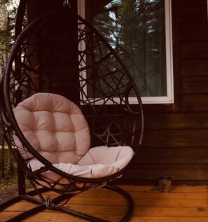 A wicker chair with a cushioned seat and back, positioned on a wooden deck. - Denali Wild Stay (Healy)