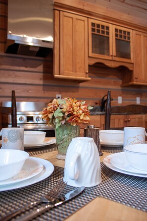 A wooden kitchen with a stove, cabinets, and a dining table set with plates, cups, and a vase of flowers. - Denali Wild Stay (Healy)