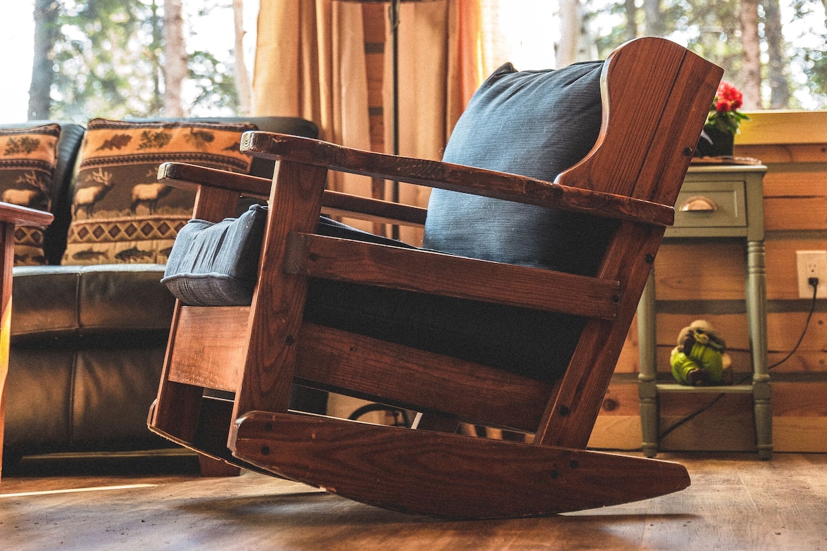 A wooden rocking chair with a cushion, a lamp, and a window with curtains.