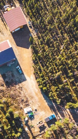 An aerial view of a rural area with a few buildings, a dirt road, and scattered vehicles. - Denali Wild Stay (Healy)