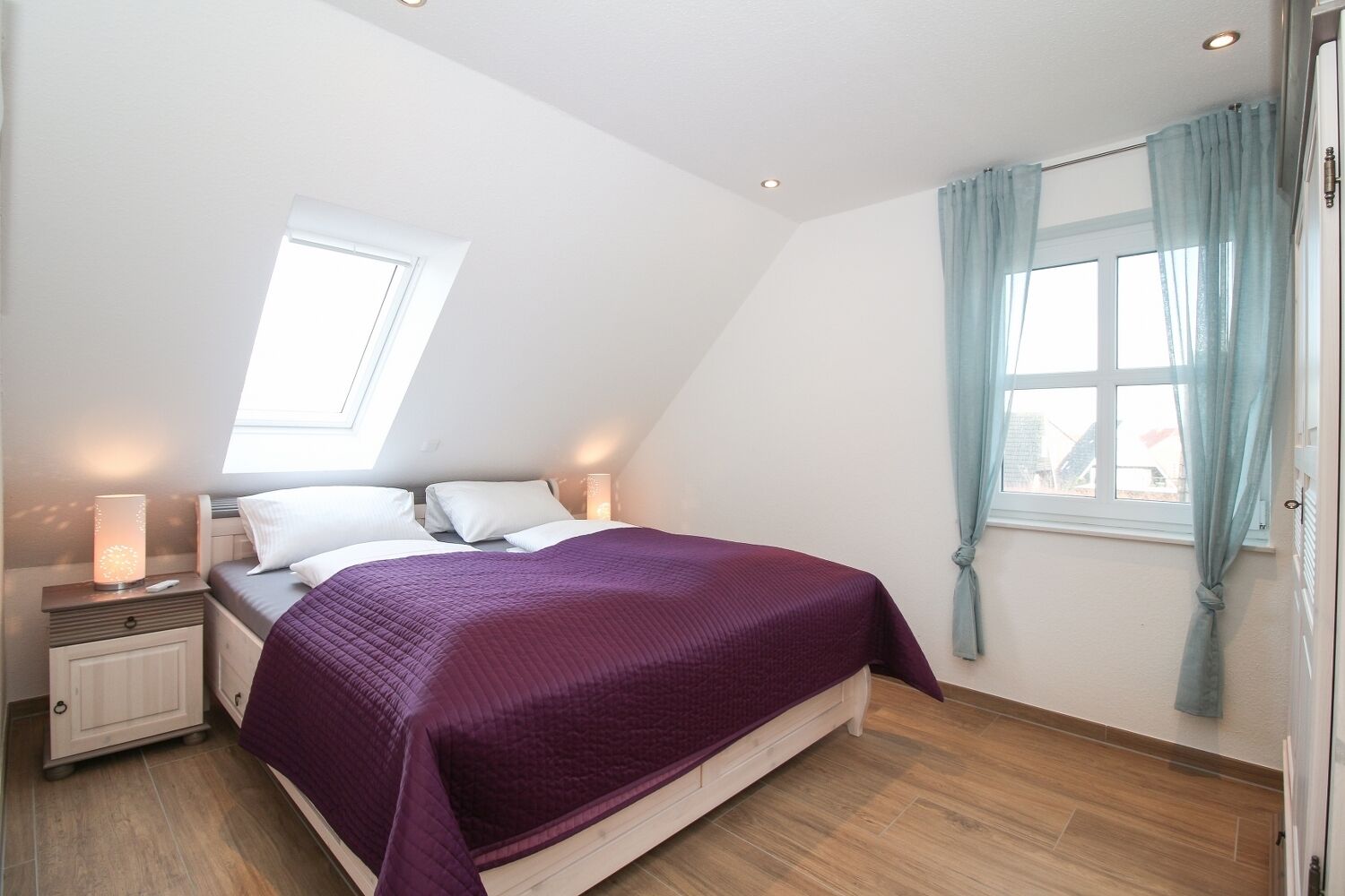 A bedroom with a bed, nightstands, a window with curtains, and a skylight.