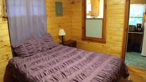 A wooden cabin room with a bed, a nightstand, a lamp, a window, and a door leading to a bathroom. - #4 Adirondack FamilyFriendly Waterfront on LoonLake. Boating,fishing,swimming!  (Chestertown)