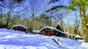 A cabin-style hotel with multiple buildings, each featuring a red exterior and large windows. There is a snow-covered landscape with a staircase leading to the buildings. - #4 Adirondack FamilyFriendly Waterfront on LoonLake. Boating,fishing,swimming!  (Chestertown)