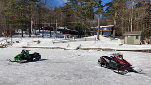 Two snowmobiles parked on a snowy surface with a building and trees in the background. - #4 Adirondack FamilyFriendly Waterfront on LoonLake. Boating,fishing,swimming!  (Chestertown)