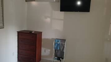 Une pièce avec une commode en bois, un climatiseur fixé au mur et un téléviseur.