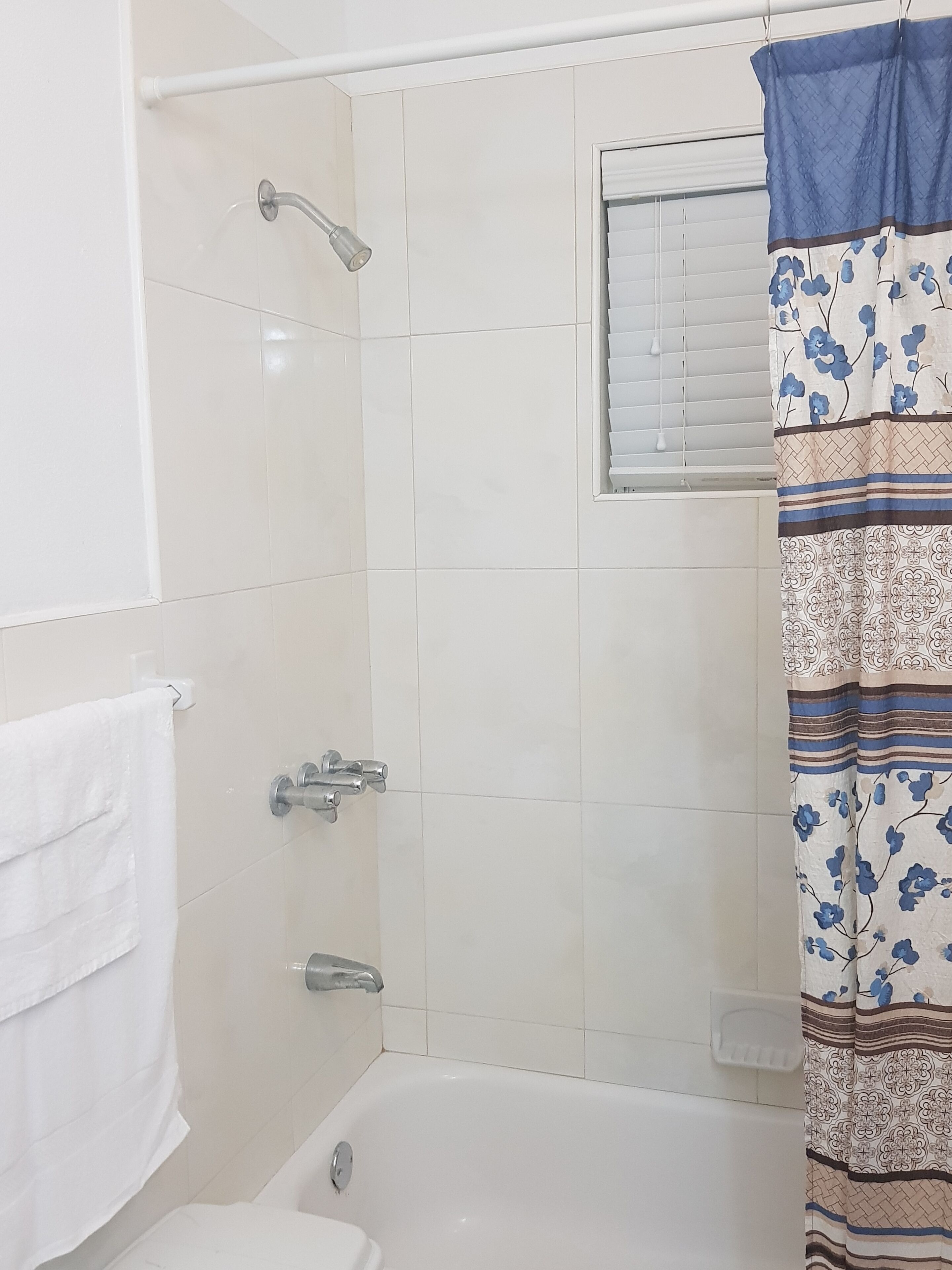 A bathroom with a shower, a toilet, and a window with blinds.