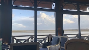 Une pièce dotée de grandes fenêtres donnant sur une plage, et aménagée avec des chaises et des tables.