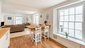 A spacious living area with a wooden dining table, white chairs, a sofa, and a large window. - 2 Bed in Appledore (oc-loblof) (Appledore)