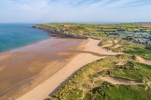 An aerial view of a coastal area with a sandy beach, green fields, and a small settlement with buildings. - 4 Bed in Croyde (oc-bfarmh) (Croyde)