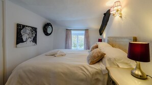 Quarto de hotel com cama, abajur, relógio na parede, janela com cortinas e um quadro na parede.