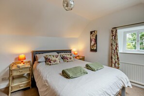 A bedroom with a bed, two bedside tables, a window with curtains, and a wall-mounted artwork.