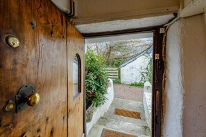 A wooden door with a brass handle, leading to a stone staircase and a white wall with greenery. - 4 Bed in Croyde (oc-bfarmh) (Croyde)