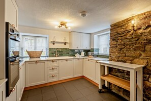 A modern kitchen with white cabinets, a stone accent wall, and a built-in bench.