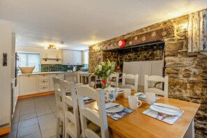 A dining area with a wooden table set for four, white chairs, and a stone wall backdrop.