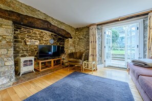 Une pièce aux murs de pierre, équipée d’une télévision, d’une cheminée, d’un canapé et d’une grande fenêtre.