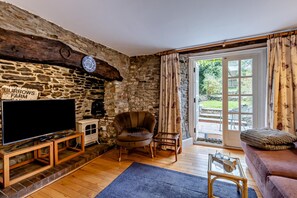 A cozy living room with a stone wall, a flat-screen TV, a comfortable armchair, and a sofa.