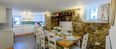 Comedor con pared de piedra, sillas blancas y una mesa lista para cuatro.