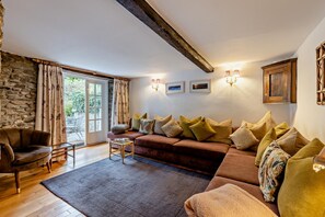 Ein gemütliches Wohnzimmer mit einer Steinwand, einem braunen Sofa mit Kissen, einem Holztisch und Blick ins Freie durch eine Glastür.