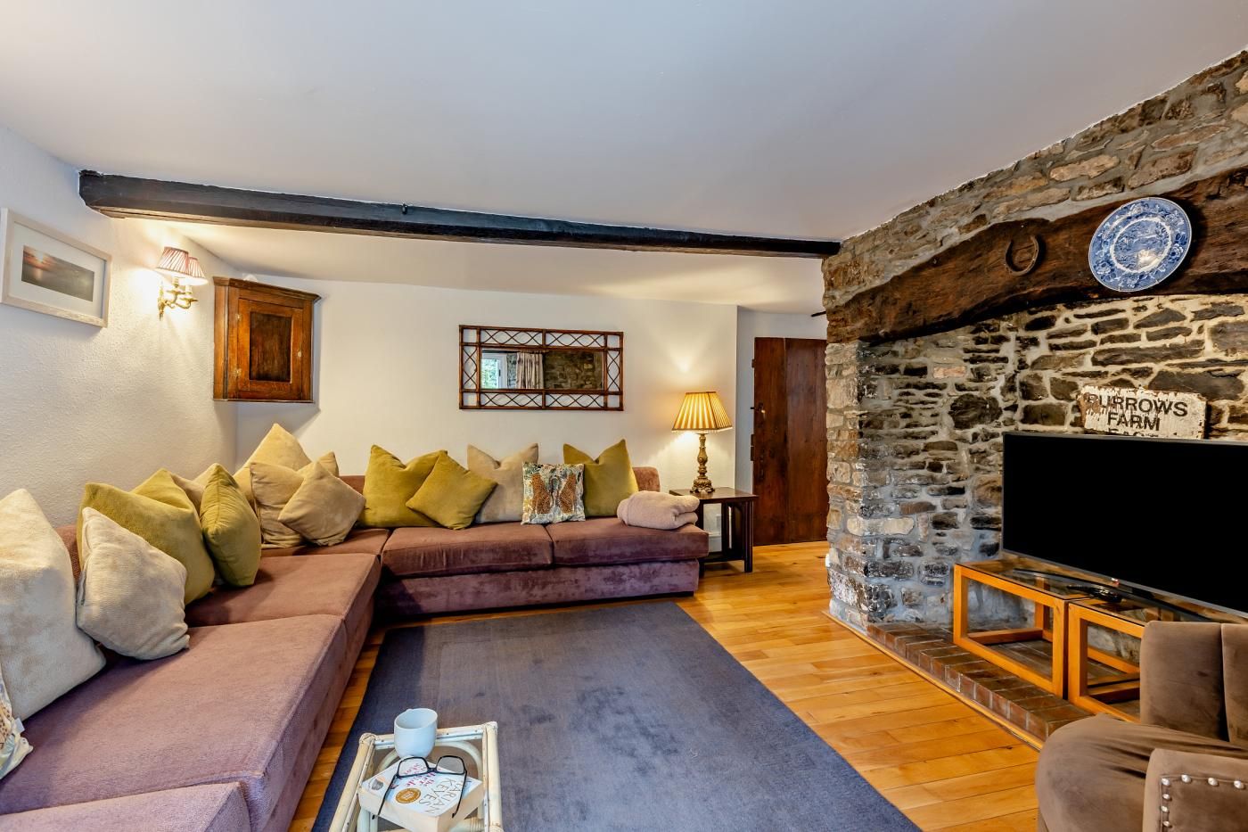 Ein gemütliches Wohnzimmer mit Kamin aus Stein, einer Couch mit Kissen, einem Fernseher und einem kleinen Tisch mit Tasse und Gläsern.