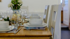 Uma mesa de jantar posta com pratos, tigelas e copos brancos, com um vaso de flores ao fundo.