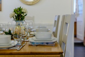 A dining table set with white plates, bowls, and glasses, with a vase of flowers in the background.