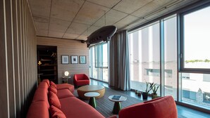 A modern lounge area with red seating, large windows, and a ceiling-mounted projector. - THE CLOUTH (Cologne)