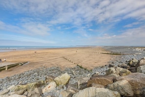 A beach with a rocky foreground and a sandy area with people walking.
