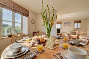 A dining area with a table set for breakfast, including plates, glasses, and a vase with flowers.