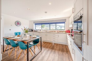 Una cocina moderna con armarios blancos, un comedor con sillas color turquesa y un amplio ventanal con vistas.