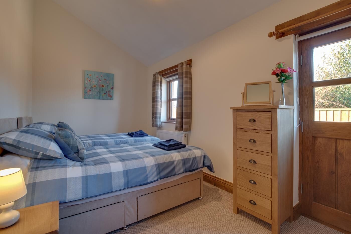 Une chambre à coucher avec un lit, une commode, une fenêtre avec des rideaux, un radiateur et un tableau accroché au mur.